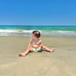 Toddler sitting on the sand beside the Atlantic Ocean during an Outer Banks family vacation